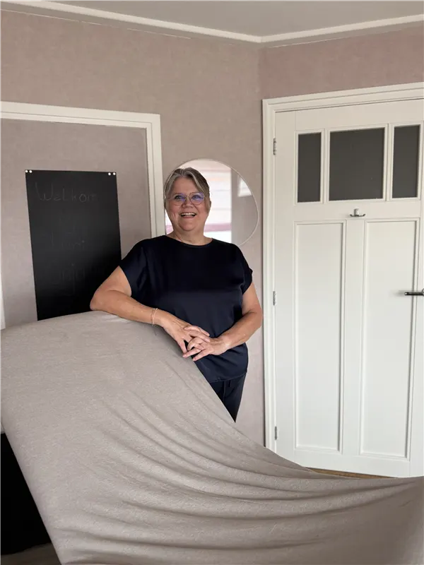 Anja van Lanen staat lachend achter de behandeltafel in haar praktijk in Uden